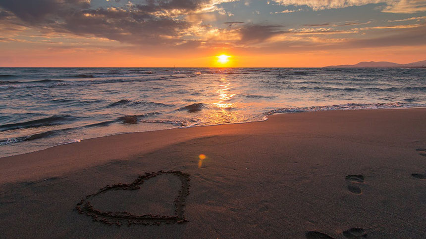 A heart drawn in the sand on a sunset beach.