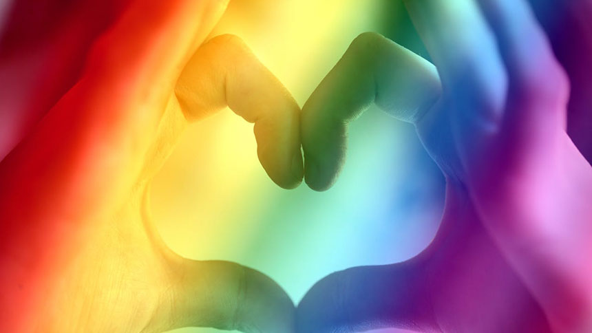 A picture of hands making a heart symbol with rainbow colors.