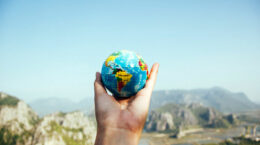 A picture of a hand holding a globe with a blue sky and mountains in the background.